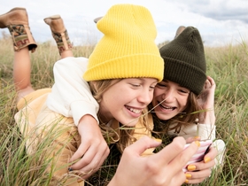 Девочки лежат на траве, улыбаются и смотрят в смартфон