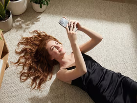 Девушка лежит на ковре и смотрит в телефон и улыбается