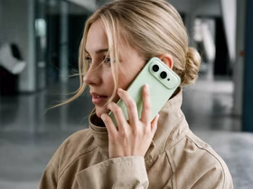 Девушка в бежевой куртке держит у уха зелёный смартфон Honor 600