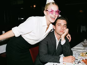 Весёлая девушка обнимает грустного парня, сидящего за столом