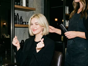 Девушка в кресле у парикхмахера показывает пальцами сердечки