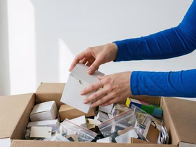 Человек достаёт маленькую белую коробочку из большой картонной коробки