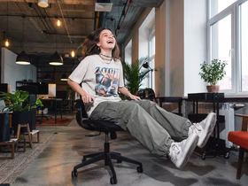 Молодая девушка зумер со счастливым лицом сидит на стуле в офисе