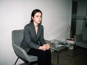 Девушка в деловом костюме сидит на стуле в кабинете офиса