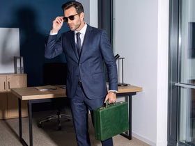 Мужчина в костюме и очках идёт с чемоданом документов