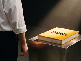Книга с логотипом «Яндекс» лежит на металлическом постаменте под направленным светом, рядом стоит человек в белой рубашке