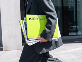 Человек в деловом костюме держит папку с логотипом Nebius и документами на фоне офисного здания