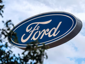 Логотип автопроизводителя Ford на синей овальной вывеске на фоне неба