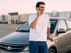 Мужчина разговаривает по телефону рядом с автомобилем Lada на парковке