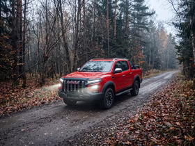 Красный JAC T9 едет по дороге через лес