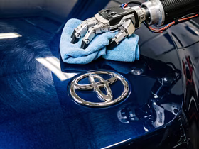 Рука робота протирает тряпкой капот автомобиля Toyota
