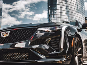 Крупный план передней части чёрного автомобиля Cadillac на фоне современного здания