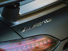 Крупный план эмблемы AMG на матовом кузове автомобиля; внизу виден край заднего фонаря
