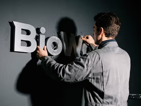 Мужчина с рабочей форме и с отвёрткой в руке снимает логотип BioWare со стены