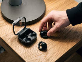 Рука человека берёт наушники Samsung Galaxy Buds On со стола