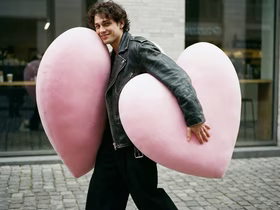 Молодой человек несёт два огромных плюшевых сердца