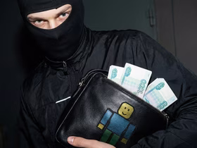 Мужчина в балаклаве с сумкой с логотипом Roblox, в которой лежат деньги