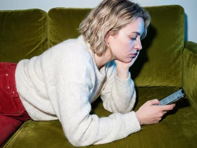 Девушка лежит на диване и смотрит в смартфон