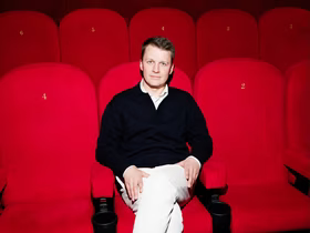 Николай Буц сидит на красном кресле в кинотеатре