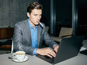 Мужчина смотрит в компьютер и держит градусник во рту