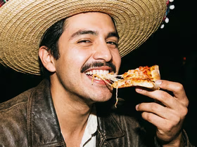 Мужчина в сомбреро ест пиццу и улыбается