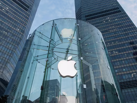 Крупный логотип Apple на стеклянном фасаде здания, окружённого небоскрёбами