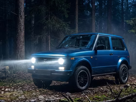 Lada Niva Legend с включёнными фарами едет по ночному лесу