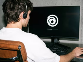 Молодой мужчина сидит за компьютером и смотрит на логотип Ubisoft на экране монитора
