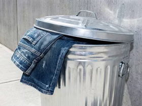 Джинсы лежат в мусорном баке