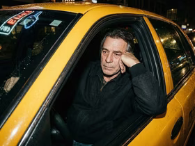 Мужчина в черной куртке сидит за рулем такси