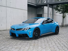 Голубая BMW iM4 рядом с серым зданием