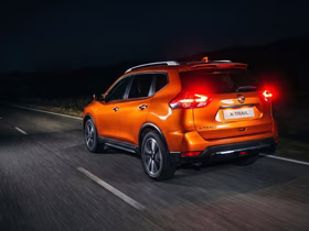 Оранжевый Nissan X-Trail едет по дороге ночью