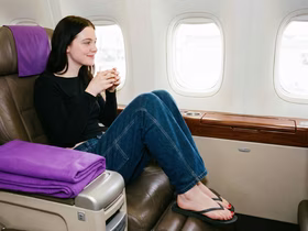 Девушка сидит в самолете в кресле с фиолетовым подлокотником