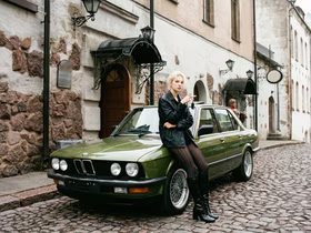 Девушка в кожаной куртке и колготках стоит рядом с зелёной BMW