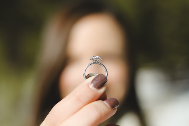 девушка держит перед лицом обручальное кольцо, размытый фон