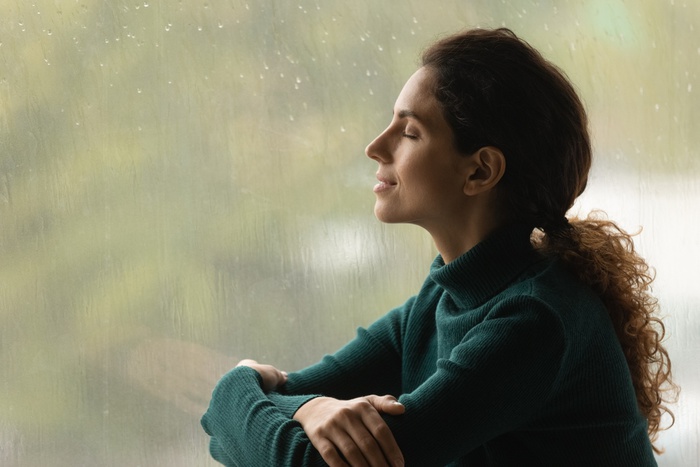 женщина сидит у окна и слушает шум дождя