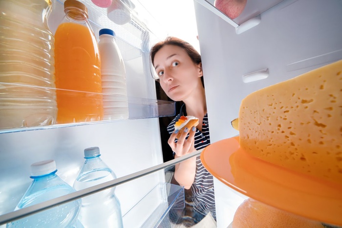 девушка берет сладости из холодильника
