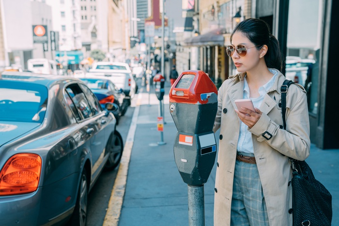 девушка подходит к припаркованному автомобилю со смартфоном в руках